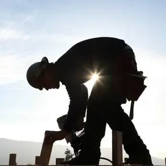 A man in black shirt and hard hat installing clean energy on top of building.