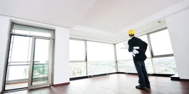 A man in a hard hat and gloves standing inside of an empty room.
