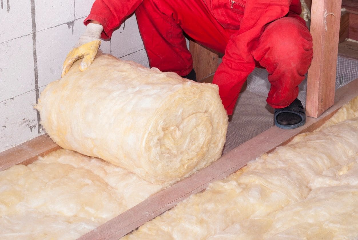 A worker in a red suit with a roll of floor insulation.