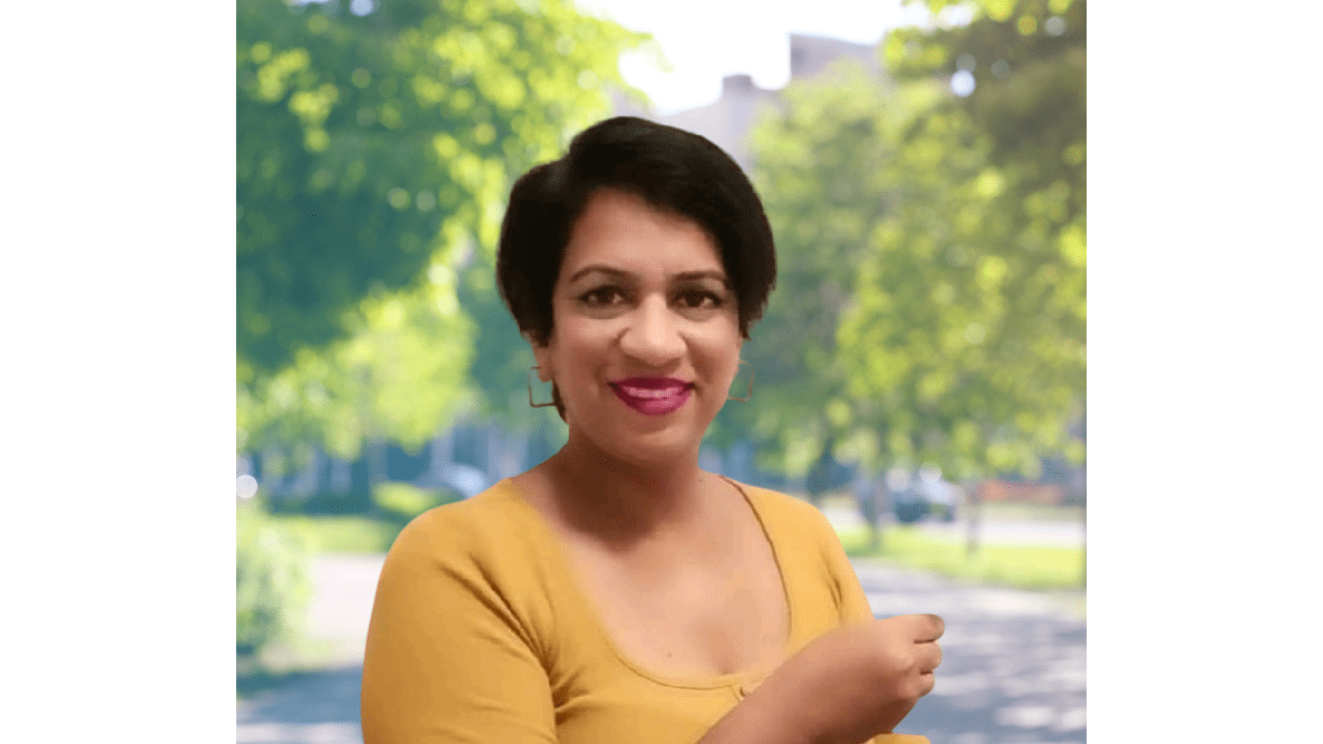 Woman in yellow shirt, smiling outdoors.